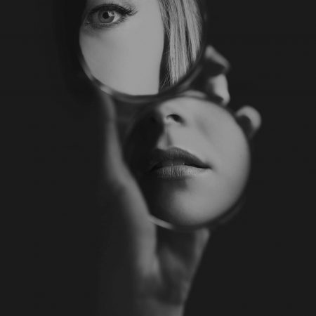 Woman looking at her eye and mouth in a small mirror artistic conversion